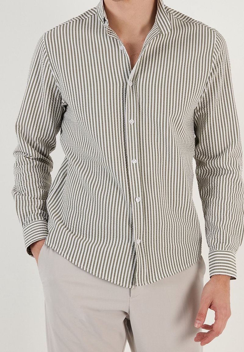 Camicia a righe verde oliva e bianca, con una vestibilità slim, maniche lunghe e colletto a punta. Tessuto liscio con una sottile texture.