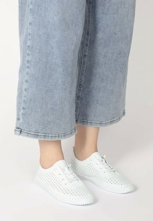 Weiße, perforierte Sneakers mit Schnürsenkeln, aus synthetischem Material, kombiniert mit weit geschnittenen, blauen, knöchellangen Jeans.