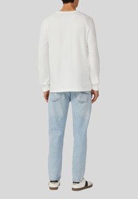 Long-sleeve white T-shirt with a crew neck, paired with light blue jeans and white sneakers. Fabric appears soft with a relaxed fit.