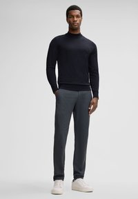 Dunkelblauer Rollkragenpullover kombiniert mit strukturierten grauen Hosen und weißen Sneakers, mit einem taillierten Schnitt und langen Ärmeln.