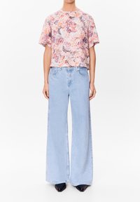 Květinový top s krátkým rukávem v broskvových a levandulových tónech, kombinovaný se světle modrými džínami s vysokým pasem a širokými nohavicemi a černými botami s špičatou špičkou.