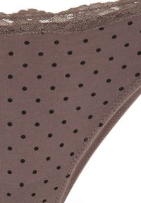 Bruine slipper met stippenpatroon en kantafwerking langs de tailleband. Het materiaal lijkt rekbaar met kleine zwarte stippen die gelijkmatig over de stof verspreid zijn.