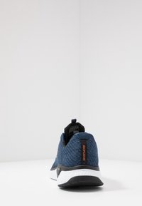 Sneaker in rete blu con tomaia strutturata, dettagli neri e suola bianca. Presenta una linguetta sul tallone e il logo del marchio sul lato.