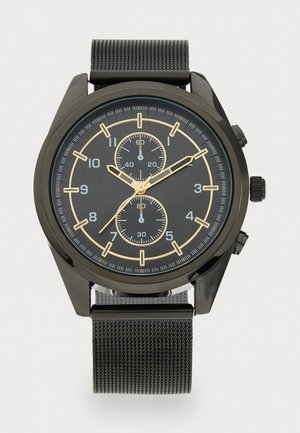 Montre en métal noir avec un cadran foncé, des accents dorés, deux sous-cadrans, des index horaires audacieux et un bracelet en maille noire texturée.