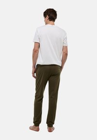 T-shirt en coton blanc et pantalon vert olive. Le pantalon possède une taille élastique et des poignets aux chevilles. Pas de motifs ni de métal visible.