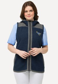 Námořnická modrá bezrukávová vesta s kapucí, šedými akcenty a zapínáním na zip. Na přední straně se nachází květinová výšivka. Měkká pletená tkanina.