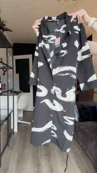Crna majica s bijelim apstraktnim uzorcima labuda, kratki rukavi, zatvaranje na gumbe i ovratnik. Izrađena od lagane tkanine.