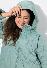 Kvadlerad mintgrön puffjacka med huva, med en framdragkedja och diamantmönster. Mjuk textur med en lätt känsla.