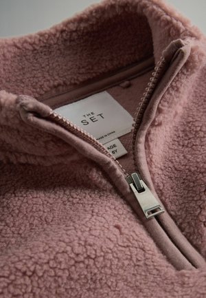 Fleecetröja i mjuk rosa med hög krage, halvdäck och texturerad yta. Lappen inuti säger "THE SET," storlek 6Y.