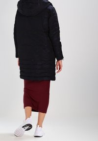 Abrigo tipo puffé en color marino con capucha, textura acolchada, costuras visibles, combinado con una falda acanalada burdeos y zapatillas blancas.