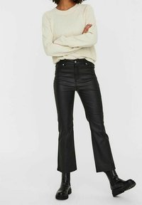 Svarta fusk läderbyxor i cropped-modell med en figurnära midja, femfickdesign och utsvängd benstil, ihop med en ljus stickad tröja och svarta stövlar.