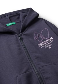 Felpa con zip di colore blu navy in materiale morbido, dotata di tasca frontale. Presenta un design grafico con testo, incluso "FREEDOM" in una tonalità più chiara.
