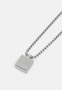 Collana d'argento con pendente quadrato dalla finitura spazzolata e logo "CK" inciso, appesa a una catena con anelli tondi.