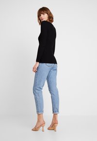 Zwarte geribbelde langemouwen top, gecombineerd met lichtblauwe opgerolde jeans en beige hakken. De outfit heeft een getailleerd silhouet.