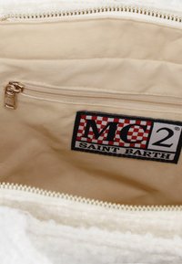 Intérieur en tissu blanc d'un sac avec une poche zippée, une texture douce et un logo brodé avec un motif à damier rouge et noir.