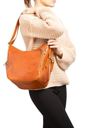 Donna con maglione beige a maglia che porta una grande borsa a tracolla in pelle marrone chiaro con dettagli di cerniera e fibbia.