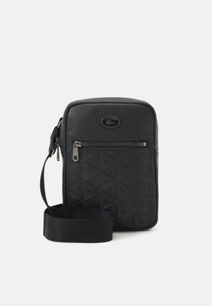 Black synthetic crossbody bag with geometric embossed pattern, zippered front pocket, branded logo, and adjustable strap.