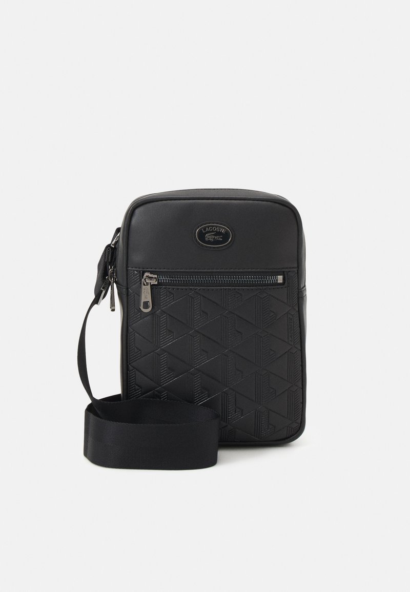 Bolsa de ombro sintética preta com padrão geométrico em relevo, bolso frontal com fecho, logotipo da marca e alça ajustável.
