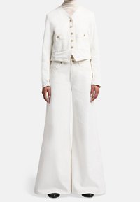 Witte denimjas met knoopsluiting en twee voorzakken, gecombineerd met bijpassende wijde broek. Gestructureerde stof en minimalistisch ontwerp.