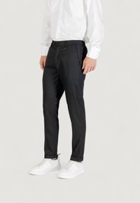 Pantalones negros ajustados con un corte slim, confeccionados en una tela suave. Presentan un frente plano, bolsillos laterales y un ligero dobladillo en el tobillo. Combinados con zapatillas blancas.