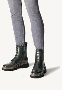 Bottines en cuir noir avec une fermeture éclair sur le côté, des accents texturés et une semelle épaisse. Associées à un jean gris clair.