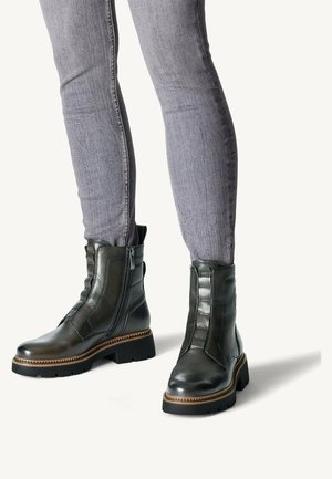 Zwarte leren enkellaarsjes met een zijrits, gestructureerde accenten en een chunky zool. Gecombineerd met lichtgrijze jeans.