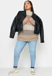 Czarna skórzana krótka kurtka na modelce, noszona na beżowym swetrze w paski, w zestawieniu z jasnoniebieskimi dopasowanymi dżinsami i szarymi sneakersami.