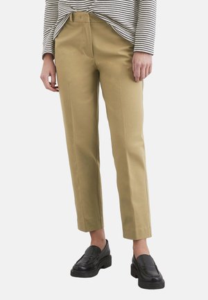 Pantaloni culotte color khaki con una superficie liscia, tasche laterali e vita aderente. Abbinati a mocassini neri e una maglietta a righe.