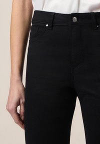Zwarte denim jeans met een slim fit, voorzien van een middelhoge taille en een voorzak. De stof heeft een gladde textuur en subtiele stikdetails.
