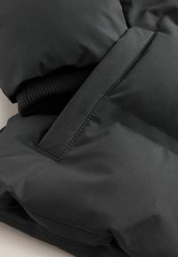 Manche de manteau d'hiver noir rembourré avec poignet en tricot côtelé et détail de poche cousu sur une surface de tissu lisse.