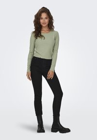 Långärmad ribbad topp i mjuk olivgrön, kombinerad med hight waist svarta skinny jeans och kraftiga svarta ankelboots.