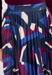 Gonna plissettata in navy, con motivi astratti in bordeaux, blu e crema. Tessuto morbido con vita elastica.