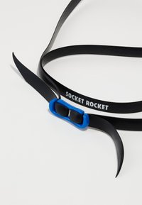 Correa de goma negra con una hebilla redondeada azul que muestra "SOCKET ROCKET" en texto blanco. Presenta extremos flexibles y puntiagudos.
