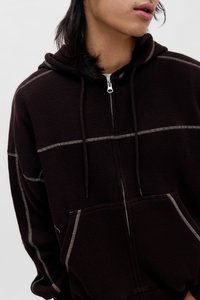 Bruine hoodie met rits en een gestructureerde stof, contrasterende stiksels, twee voorzakken en verstelbare trekkoorden aan de capuchon.