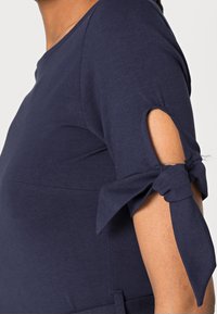 Haut bleu marine à manches courtes avec des accents noués et des détails découpés, confectionné dans un tissu doux et extensible.