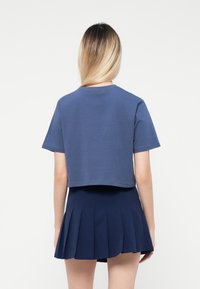 T-shirt blu accorciato con maniche corte, scollatura rotonda e texture morbida, abbinato a una gonna plissettata blu navy.