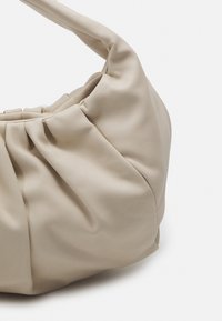 Borsa in pelle beige con texture arricciata e manico curvo. Materiale morbido e flessibile senza hardware o dettagli visibili.