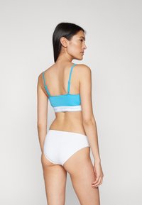 Mėlynas trumpas braletė su plonomis petnešėlėmis, turi baltą Calvin Klein logotipo juostą; derinamas su baltais hipster tipo apatiniais. Lygios audinio tekstūros.