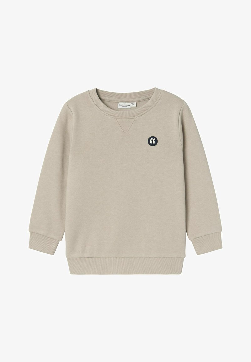 Gai krēmbalts džemperis ar garām piedurknēm, ripu vainagu un apakšmalu, kas rotāts ar mazu jūras zila krāsas izšūtu citāta zīmi uz krūtīm.