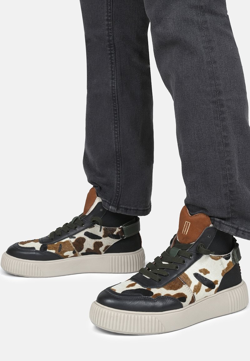 Sneaker alte con stampa di mucca, dettagli in pelle nera, suola in gomma testurizzata e lacci e tallone di un verde oliva.