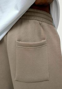 Lichtbeige sweatpants van een gestructureerde stof, met een elastische tailleband en een enkele patch pocket aan de rechterkant.
