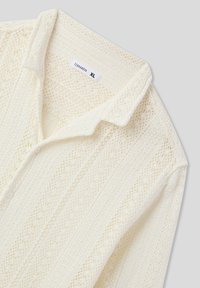 Camicia strutturata color avorio con colletto e chiusura a bottoni, caratterizzata da intricate trame a maglia e un'etichetta con la scritta "Terranova XL."