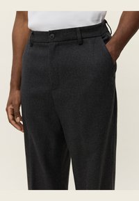 Donkergrijze broek van een gestructureerde stof, met een vlakke voorkant, riemlussen en zijzakken. Twee-knopen sluiting bij de taille.
