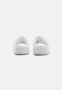 White slides with a smooth synthetic upper, rounded heel, and a textured, traction-patterned sole. Features a minimal logo detail.