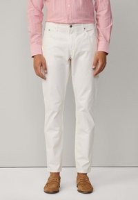 Pantalones de algodón blancos con un ajuste entallado, diseño de cinco bolsillos y cierre de botón, combinados con una camisa de rayas rosas y mocasines en color marrón claro.