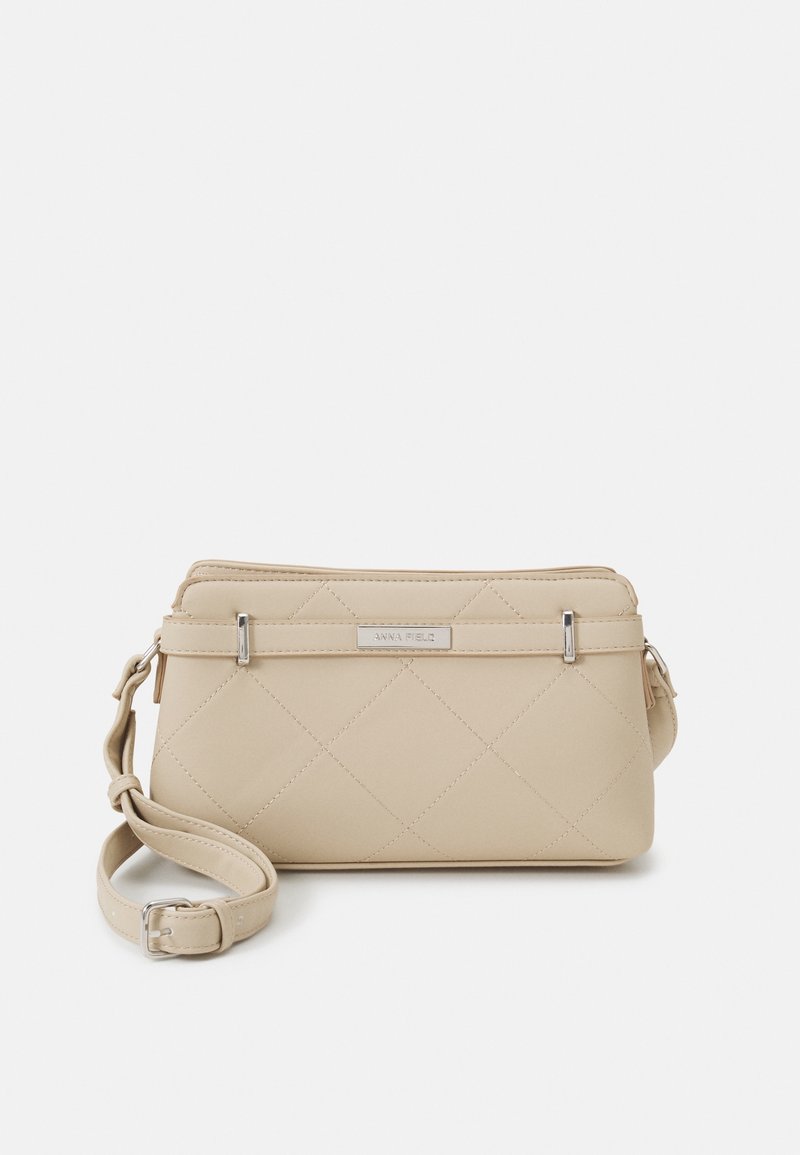 Beige prošívaná crossbody taška s hladkým povrchem, stříbrnými kovovými detaily a nastavovacími popruhy. Obsahuje značkovou kovovou destičku.