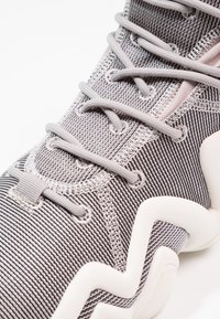 Szare buty sportowe z teksturowaną cholewką z dzianiny, falistą piankową podeszwą i płaskimi szarymi sznurowadłami. Zbliżenie ukazuje misterną stębnowanie.