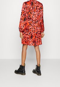 Red and pink patterned mini dress with long sleeves, tiered design, and elastic cuffs, paired with black lace-up boots.