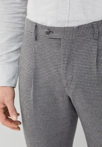 Pantaloni grigi a motivo pied de poule realizzati in tessuto strutturato, con chiusura a bottone, tasche laterali e vestibilità su misura.