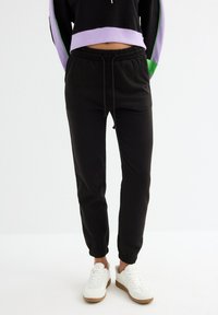 Pantalones jogger negros con cintura y puños elásticos, fabricados en suave tela de algodón. Combinado con zapatillas blancas para un look casual.